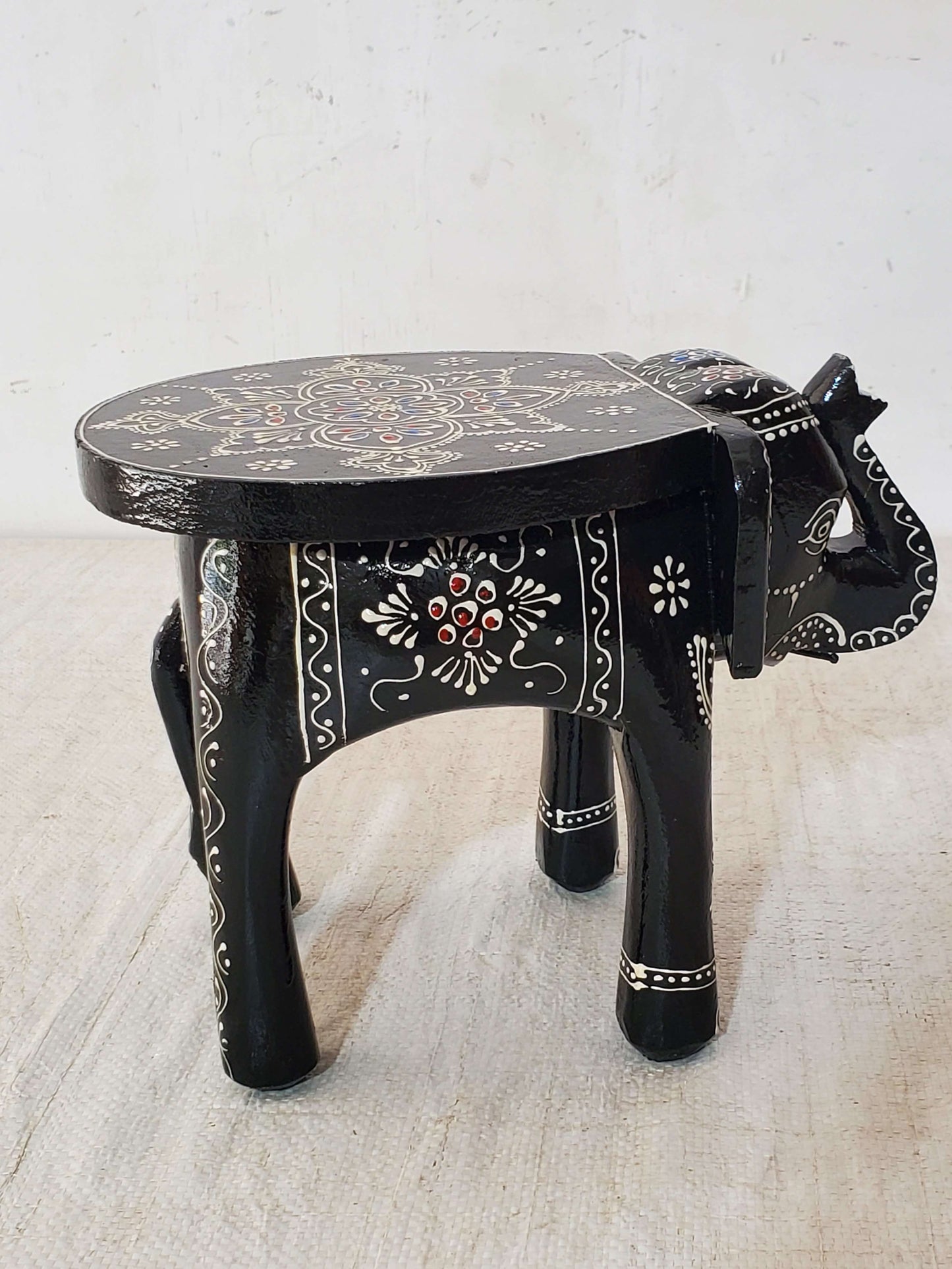 Decorative black elephant stool with intricate designs on a light background