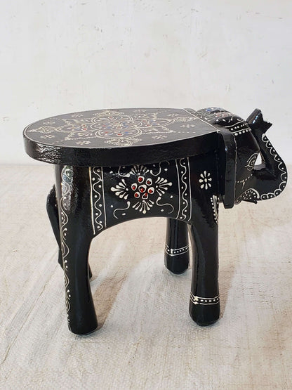 Decorative black elephant stool with intricate designs on a light background
