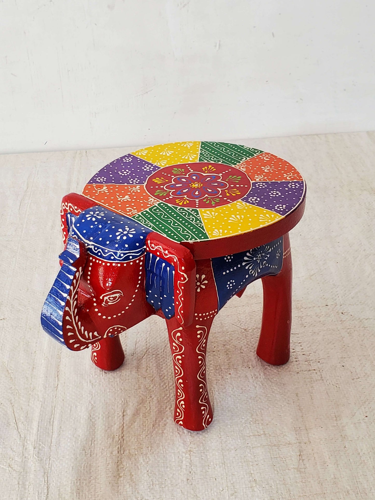 Colorful elephant-shaped stool with a rainbow pattern on a light wooden floor.